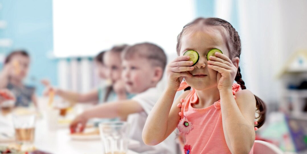 Kindergarten girl playfully holding cucumber in face